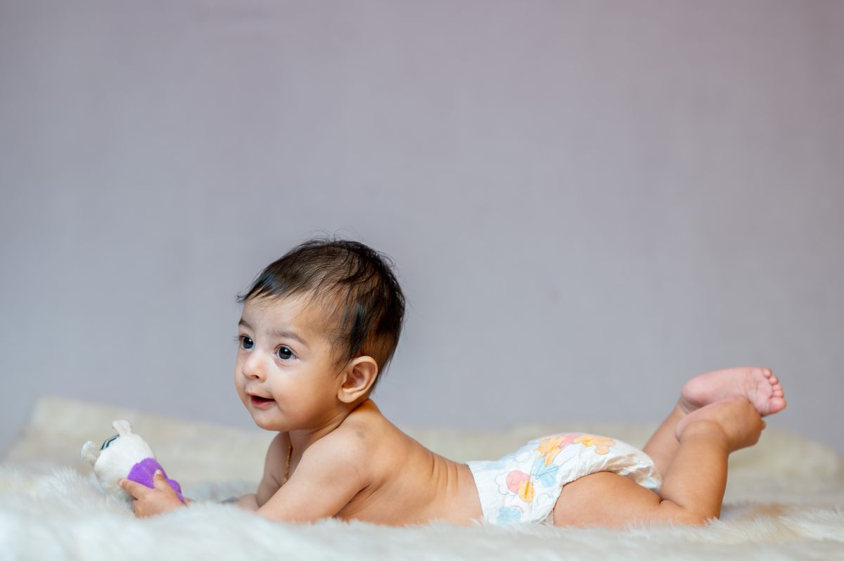 Baby in luier ligt met een speeltje op een zachte deken