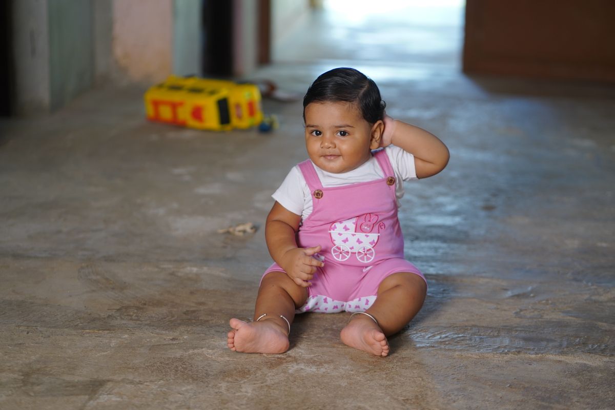 Baby in roze overall zit op de vloer met speelgoed