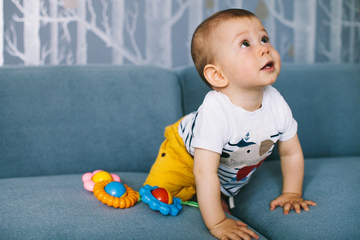 Babyjongen kruipt op een blauwe bank tussen kleurrijk speelgoed