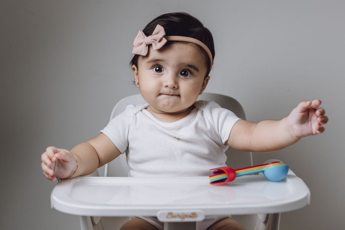 Babymeisje zit in een kinderstoel met kleurrijk speelgoedbestek