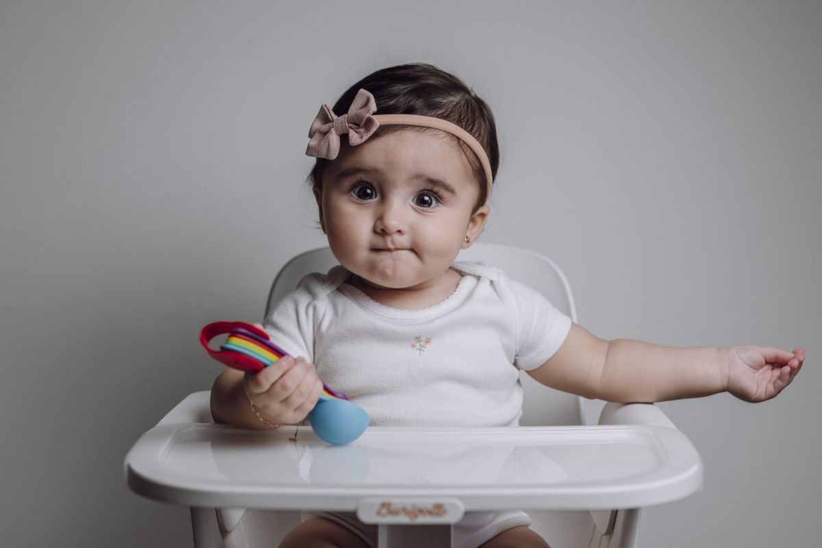 Babymeisje zit in een kinderstoel met een kleurrijk speeltje