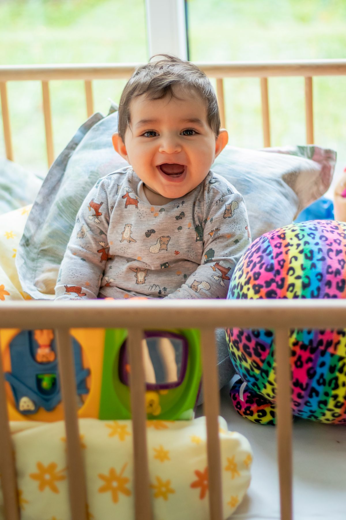 Lachende baby zit in een bedje tussen kleurrijk speelgoed
