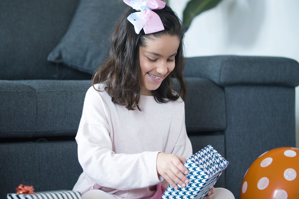 Meisje met een strik in haar haar glimlacht terwijl ze een cadeau uitpakt