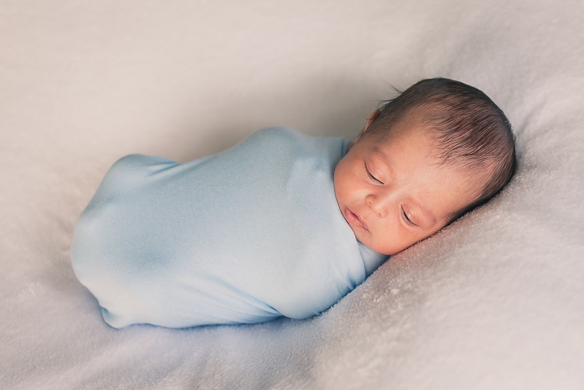 Pasgeboren baby slaapt vredig, gewikkeld in een blauwe doek