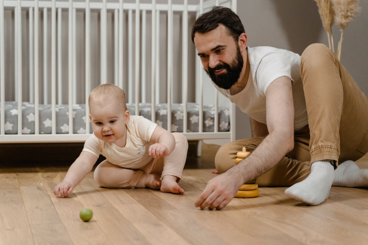 Vader speelt met zijn baby op de houten vloer van de kinderkamer